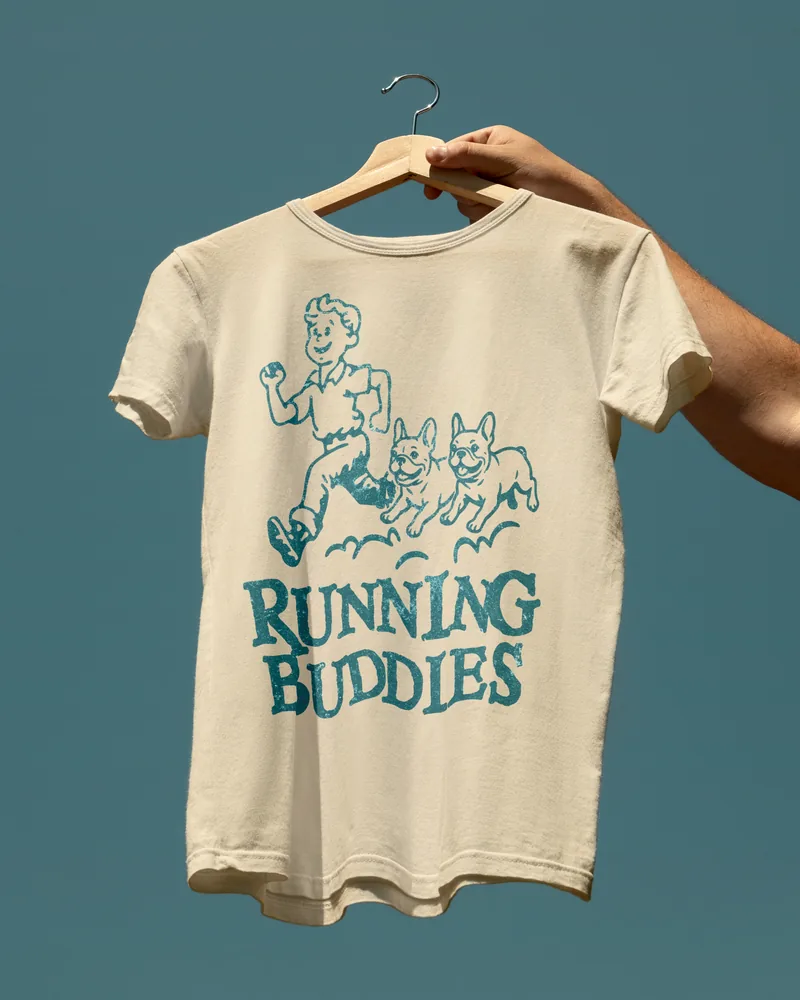 A cream tee printed with RUNNING BUDDIES and a teal drawing of a person running with three French Bulldogs.