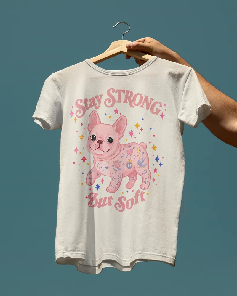 A tee printed with Stay Strong But Soft and a pink flowered French Bulldog.